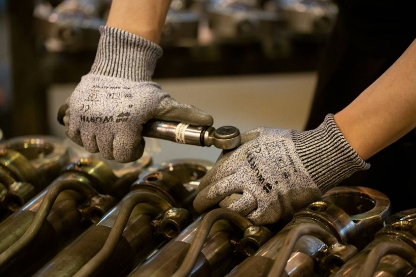 A worker wears protective gloves and tightens a screw in an industry factory.