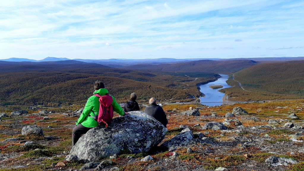 Travellers sit on a rock and watch a beautiful autumn River Tenojoki scenery in Utsjoki