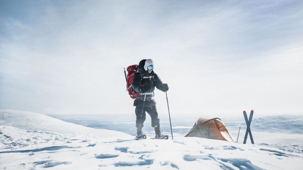 A man in outdoor gear is skiing on top of a fell in the winter