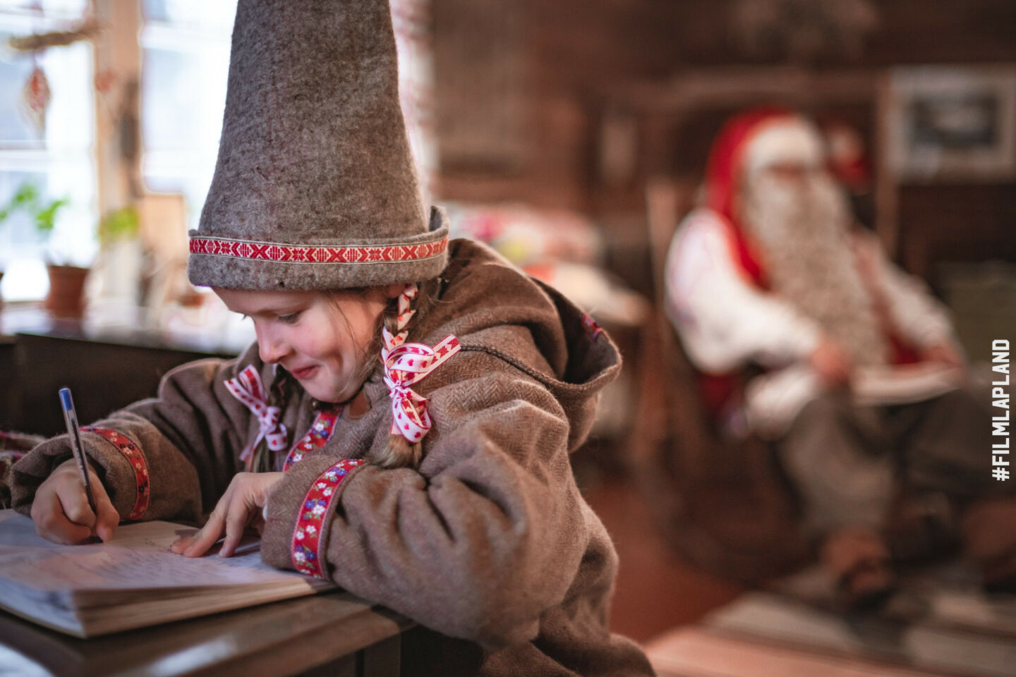 A child elf writes a letter while Santa watches in Savukoski, Finland