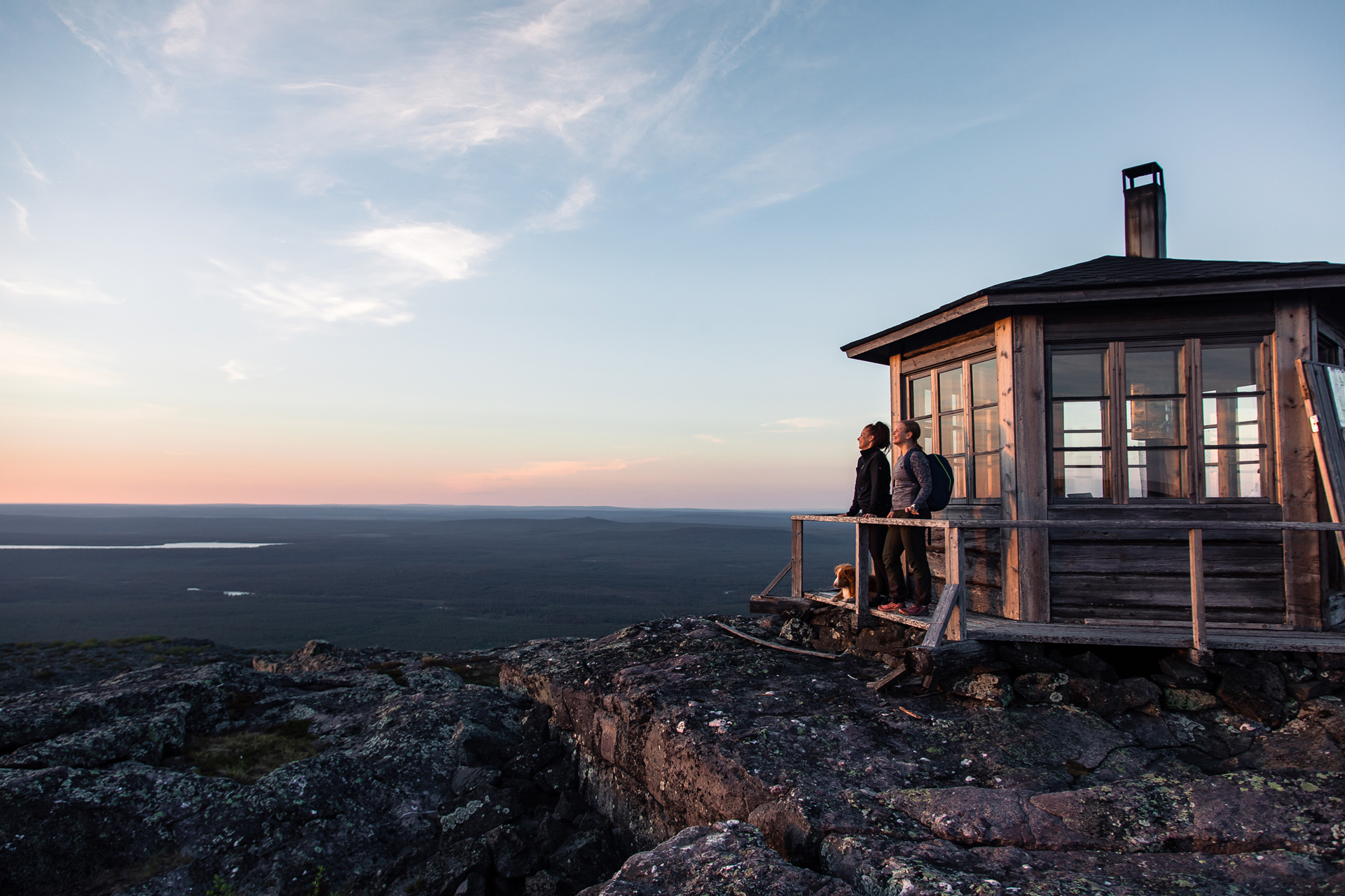 Kaksi naista katsovat tunturin huipulla auringonlaskua