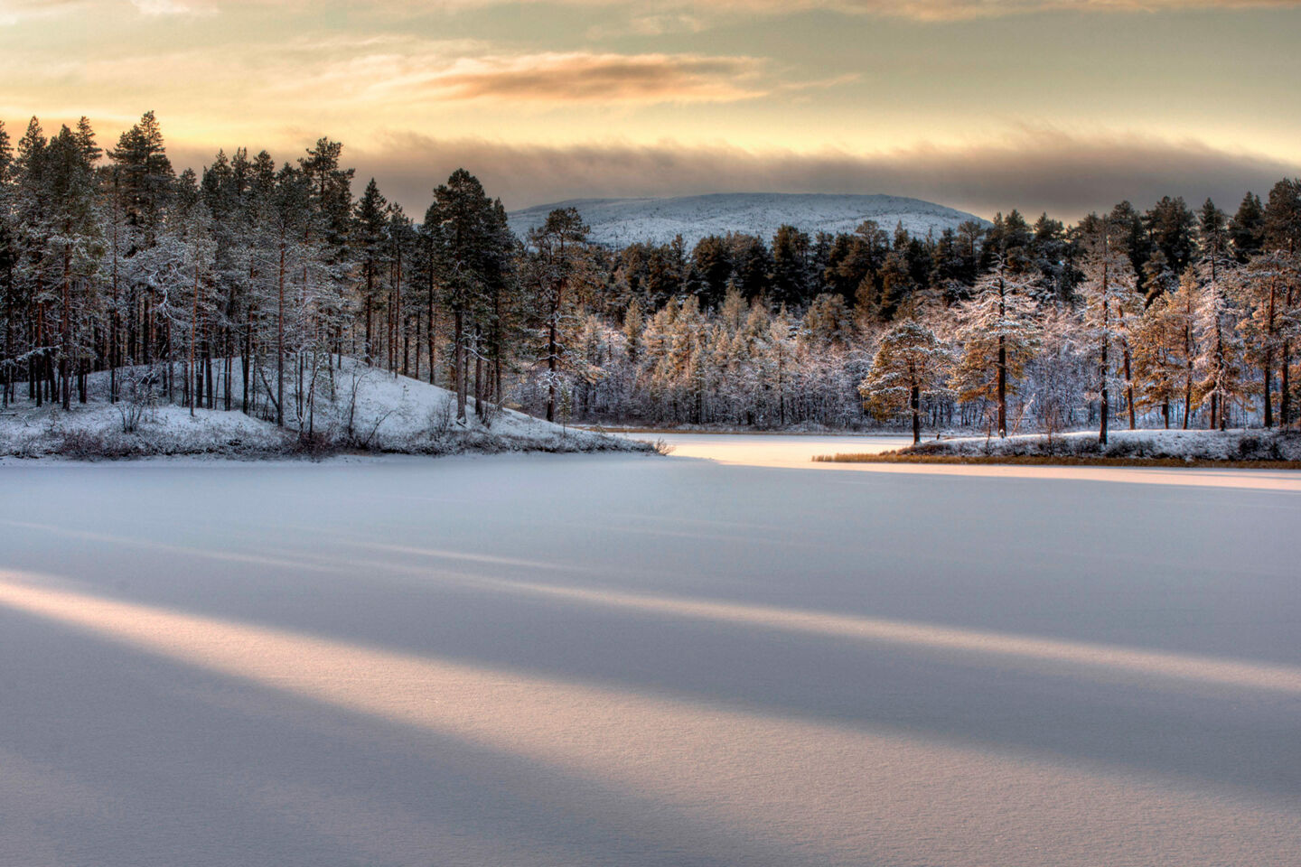 Sunbeams across the snow atop a frozen lake in Lemmenjoki National Park in Inari, Finland